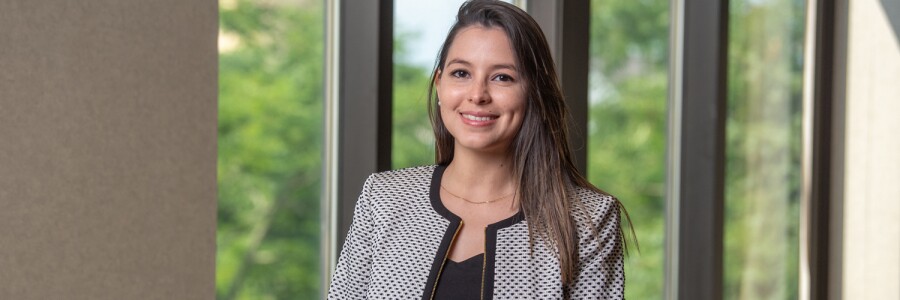 young professional smiles, stands in front of window