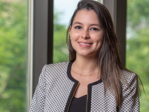 young professional smiles, stands in front of window