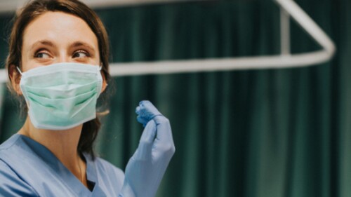 nurse with mask puts on rubber glove in patient room