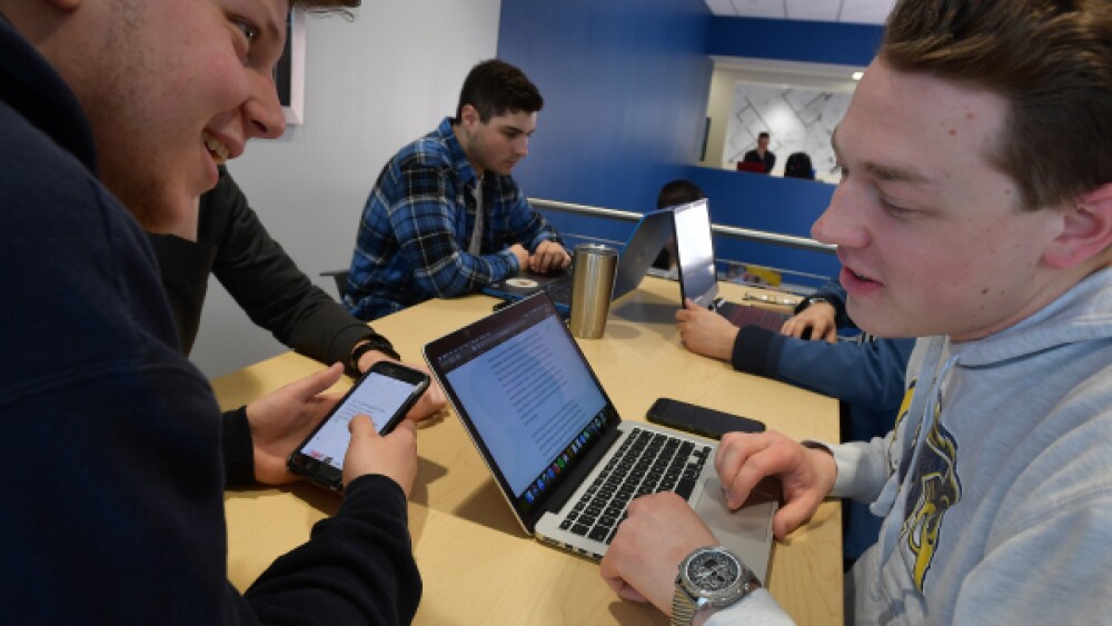 two students collaborating with laptop and phone in hands