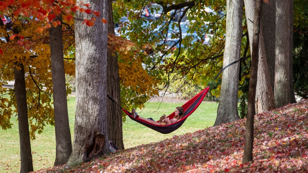 student with headphones on in hammock on a fall day
