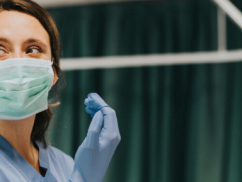 nurse with mask puts on rubber glove in patient room