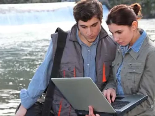 Man and woman recording research on a computer by the water