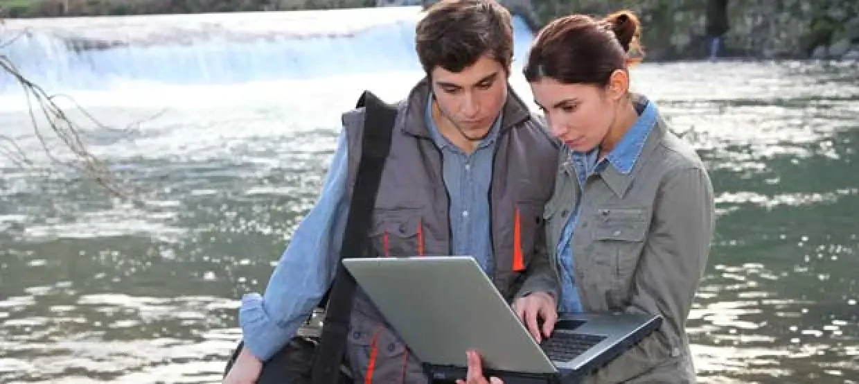 Man and woman recording research on a computer by the water