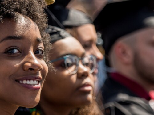 graduate in cap and gown smiles at graduation among fellow graduates