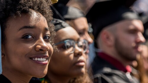 graduate in cap and gown smiles at graduation among fellow graduates