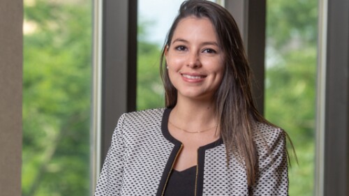 young professional smiles, stands in front of window