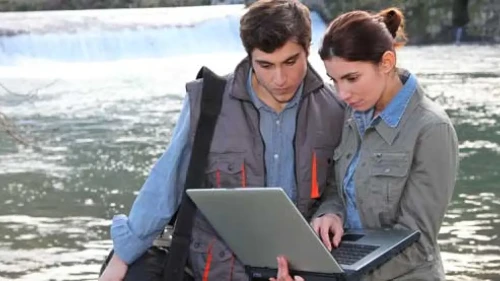 Man and woman recording research on a computer by the water