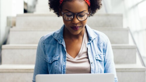 casually dressed student sits on stairs and works on laptop