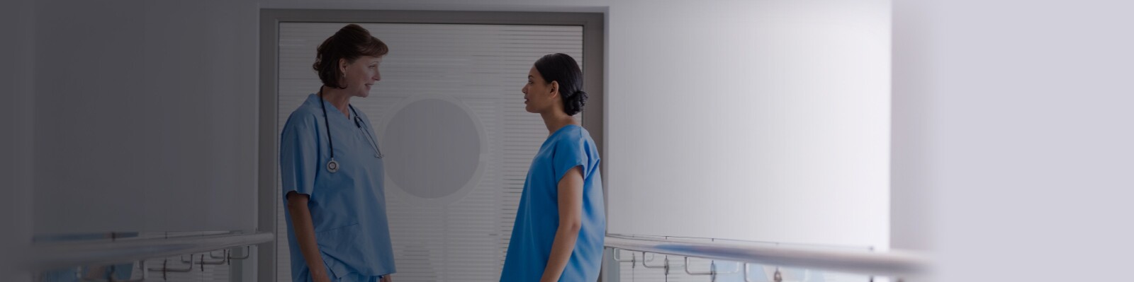 two nurses in blue scrubs converse in a hallway