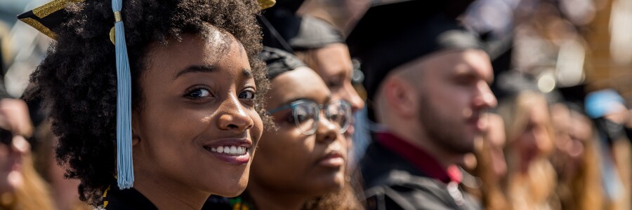 graduate in cap and gown smiles at graduation among fellow graduates