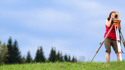 surveyor on a hill, trees in the background
